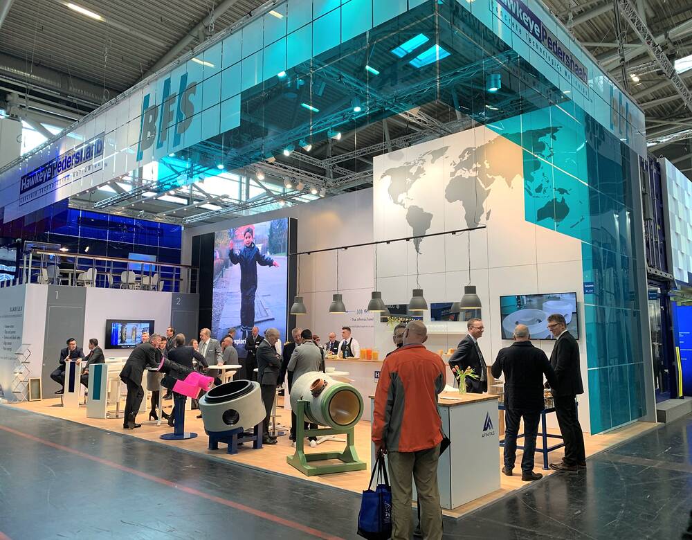 Stor specialdesignet messestand på industrimesse med besøgende, produkter og markant blå overbygning.